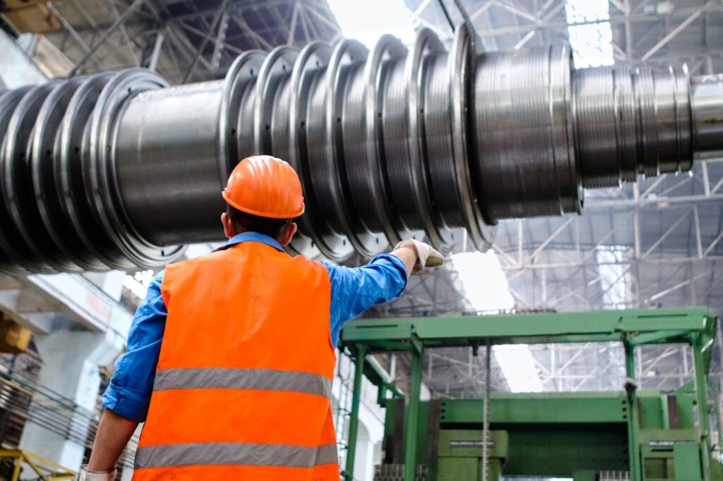 pexels-photo-2760241 Engineer in high visibility vest and hard hat inspecting large machinery in factory setting.
